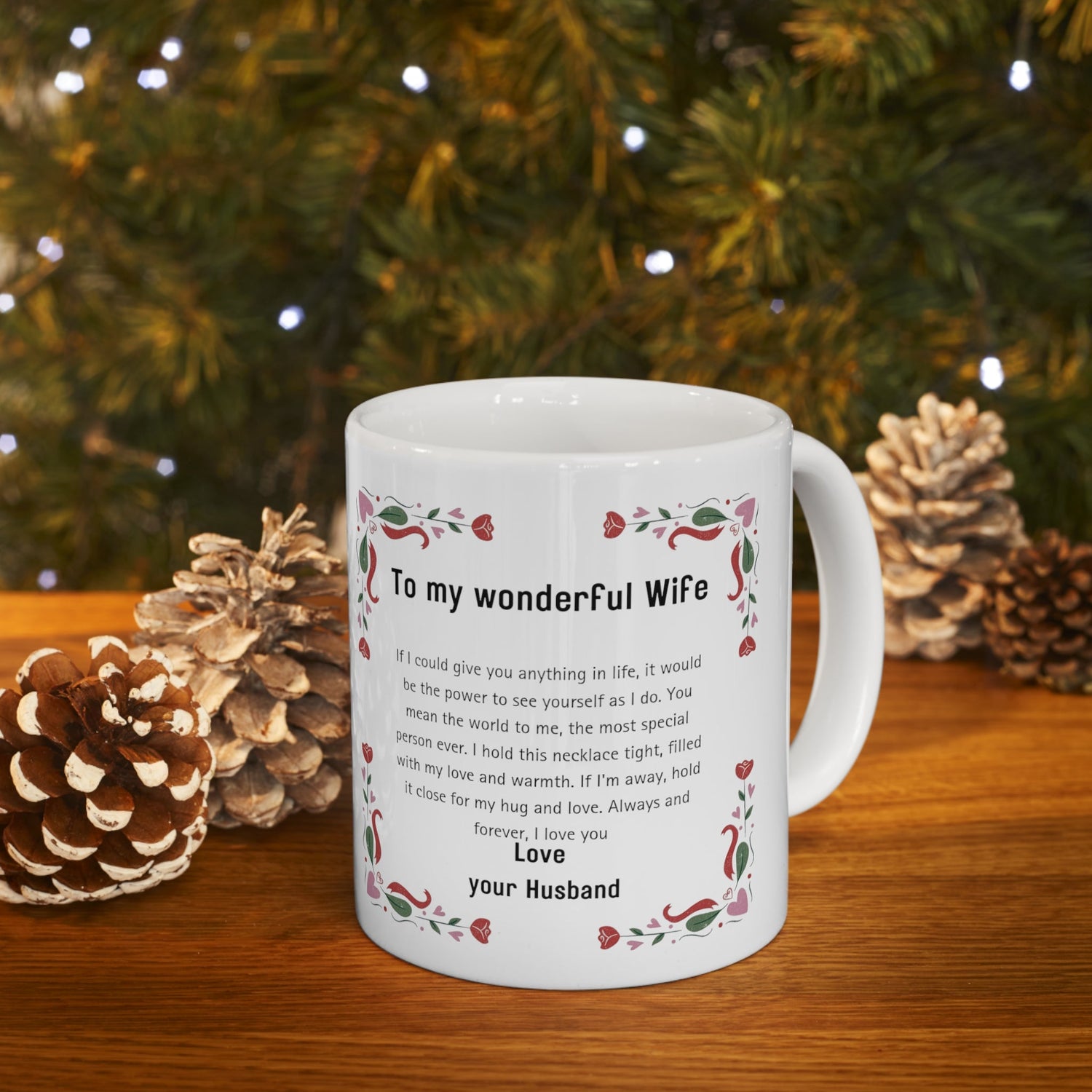 A mug with a loving message for a wife from her husband, surrounded by pine cones, with a blurred christmas tree in the background.