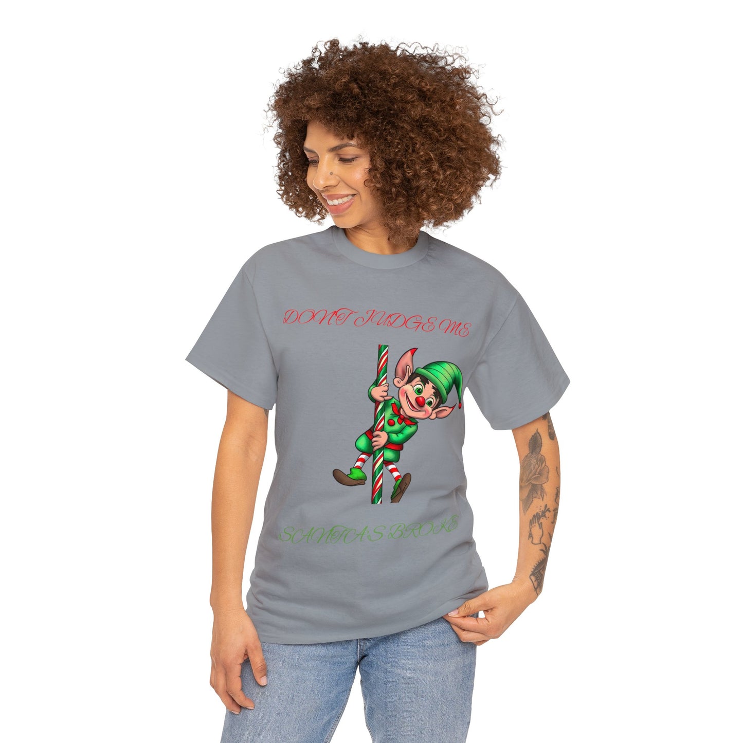 A person wearing the Unisex Heavy Cotton "Don't Judge Me Elf" shirt in gray, featuring a festive elf design and the phrase "Don't Judge Me, Santa Does", made from 100% cotton for a classic fit.