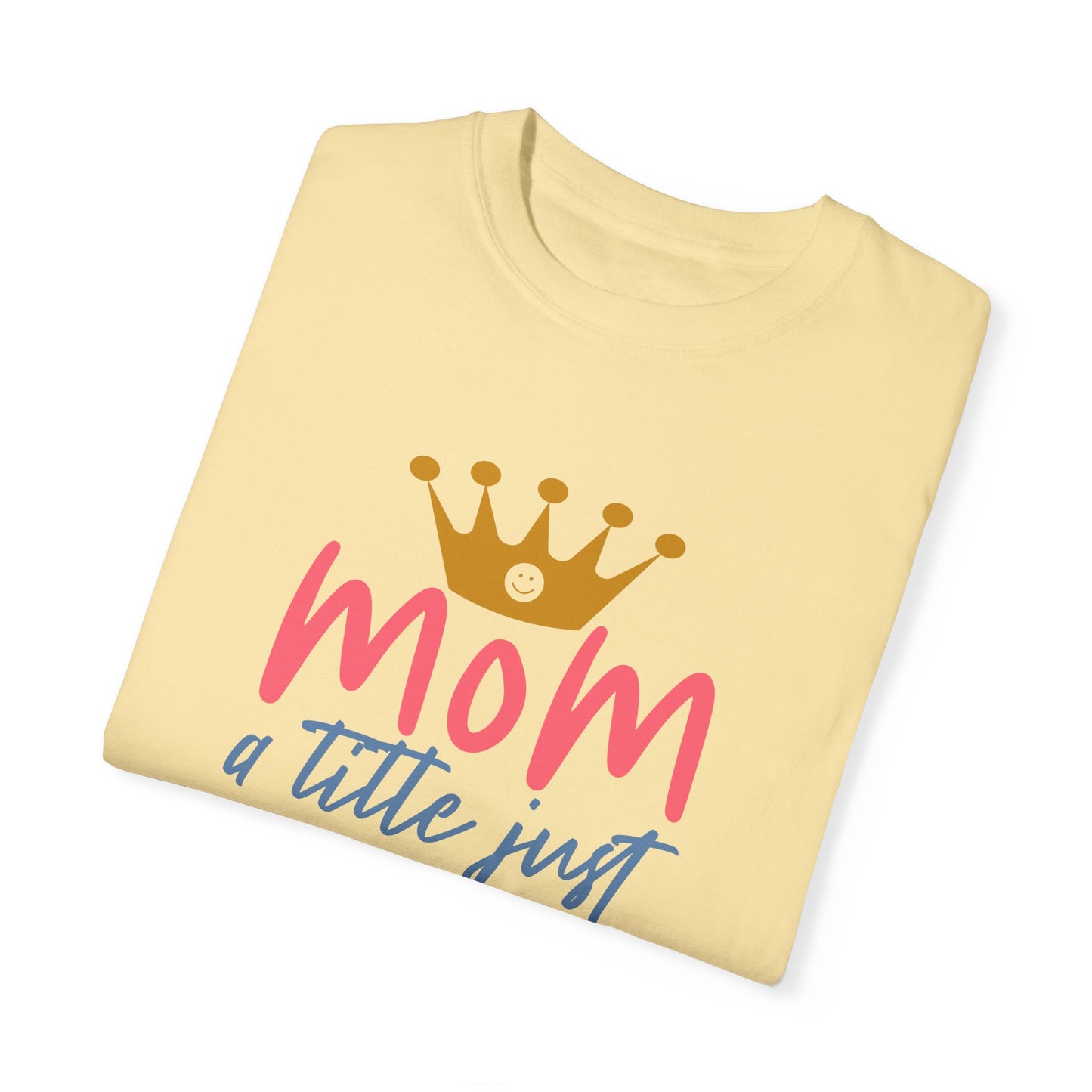 The Stylish Comfort with Unisex Comfort Colors 1717 Garment-Dyed T-Shirt features a folded yellow design with "mom" in pink letters and a crown illustration above. Accompanying the design, the text reads "just a little above queen" in blue. Made from soft, ring-spun cotton, this tee ensures unmatched comfort and style.