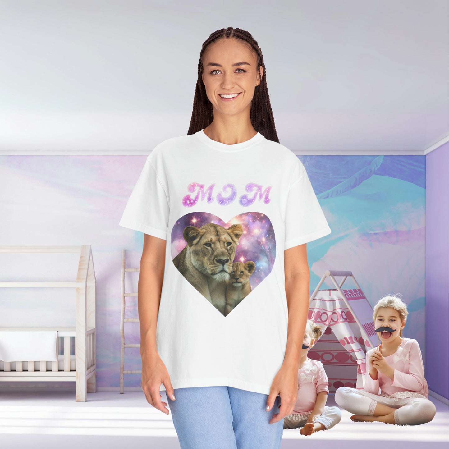 A woman in a Stylish Comfort with Unisex Comfort Colors 1717 Garment-Dye- T-shirt- Heart of the Cosmos: Mom's Lioness Legacy tee with a lion and cub inside a heart print, standing in a room with a child playing in the background.