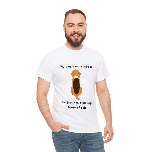 A man wears a Unisex Heavy Cotton Tee featuring a cartoon dog illustration and the text, "My dog is not stubborn, he just has a strong sense of self.