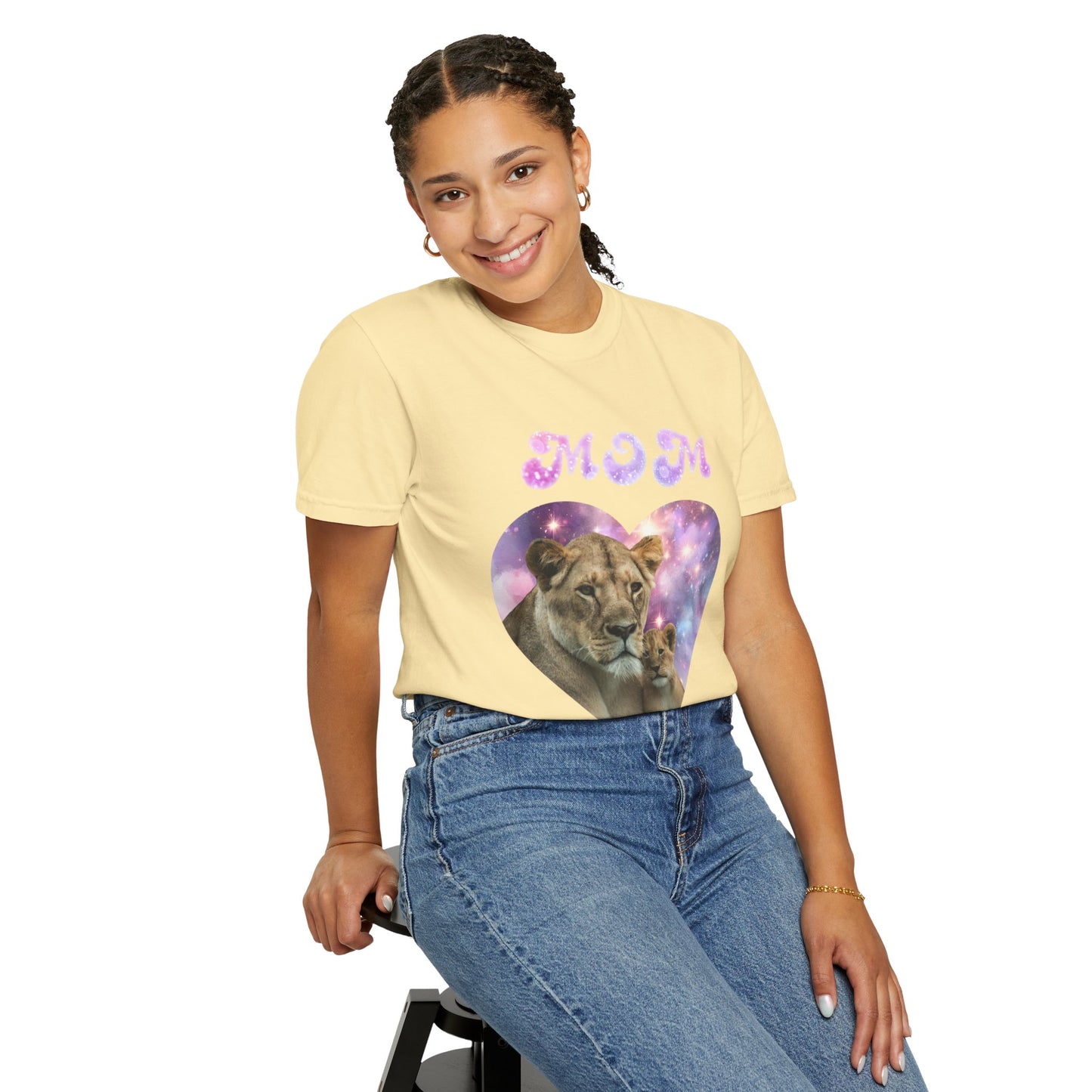 A woman sits on a stool, wearing a vibrant yellow "Heart of the Cosmos: Mom's Lioness Legacy" t-shirt from the Stylish Comfort Unisex Comfort Colors 1717 collection. The colorful heart and lioness design perfectly complements her blue jeans, while the 100% ring-spun cotton fabric offers both garment-dyed style and comfort.