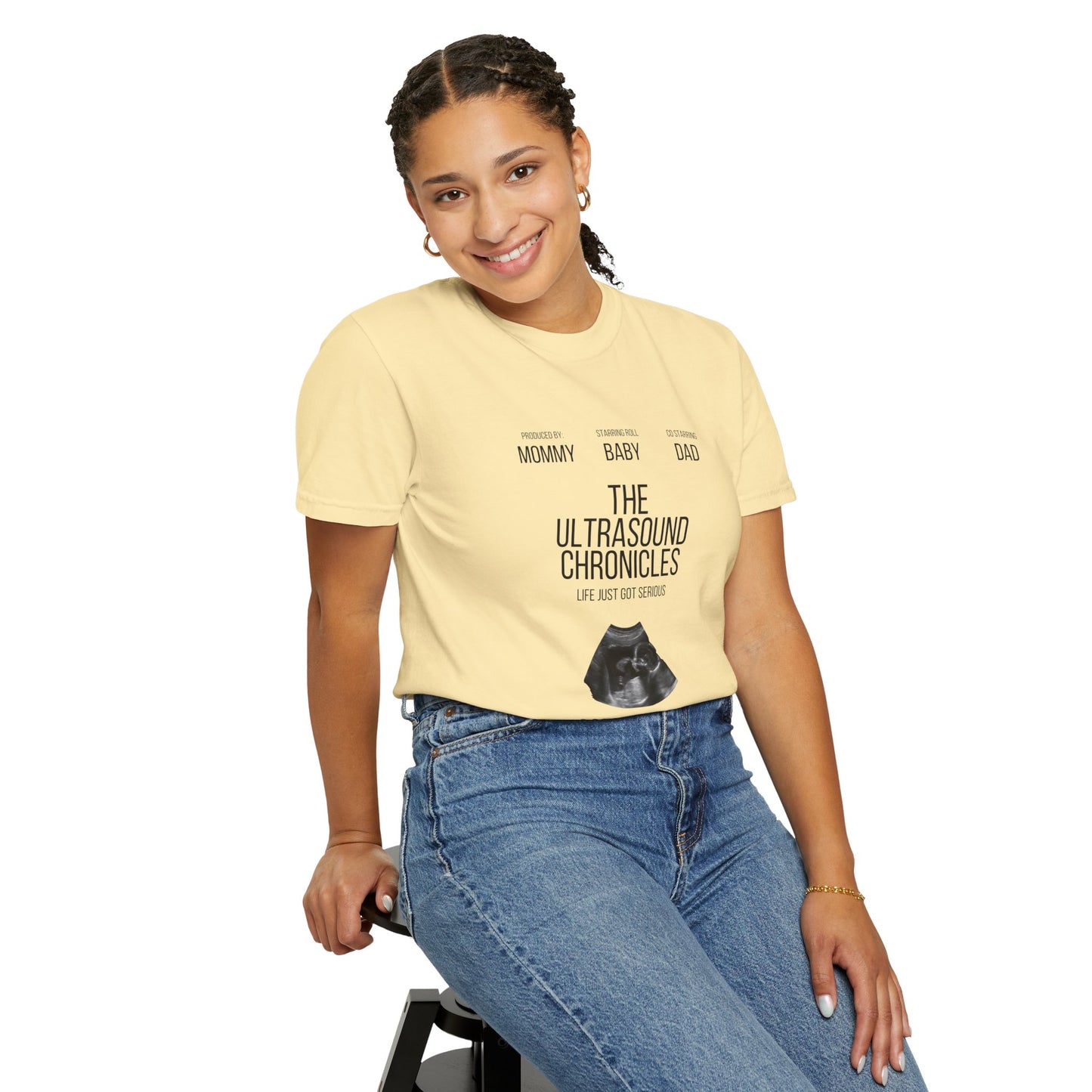 Sitting on a stool and smiling at the camera, the person is wearing "Stylish Comfort with Unisex Comfort Colors 1717 Garment-Dye T-shirt - The Ultrasound Chronicles," masterfully crafted from soft ring-spun cotton that effortlessly combines style and comfort.