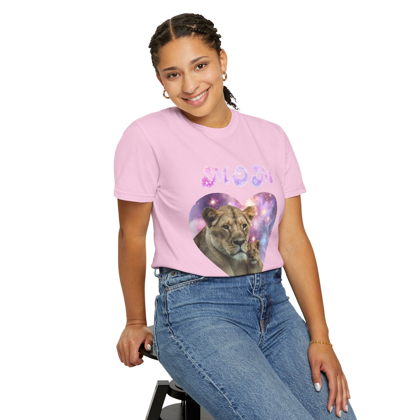 A person wearing a pink Stylish Comfort with Unisex Comfort Colors 1717 Garment-Dye T-shirt, showcasing the Heart of the Cosmos: Mom's Lioness Legacy design, sits on a stool and smiles against a plain white background. Made from 100% ring-spun cotton, this garment-dyed tee seamlessly blends style and comfort.