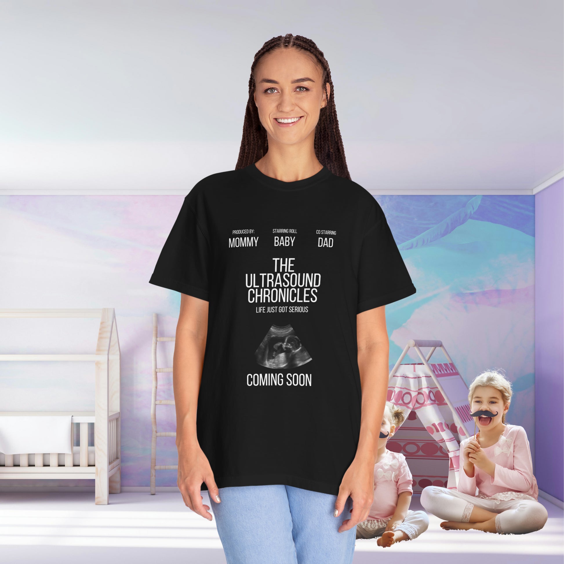 A woman in a Stylish Comfort with Unisex Comfort Colors 1717 Garment-Dye- T-shirt- The Ultrasound Chronicles smiles, with children playing in a nursery behind her.