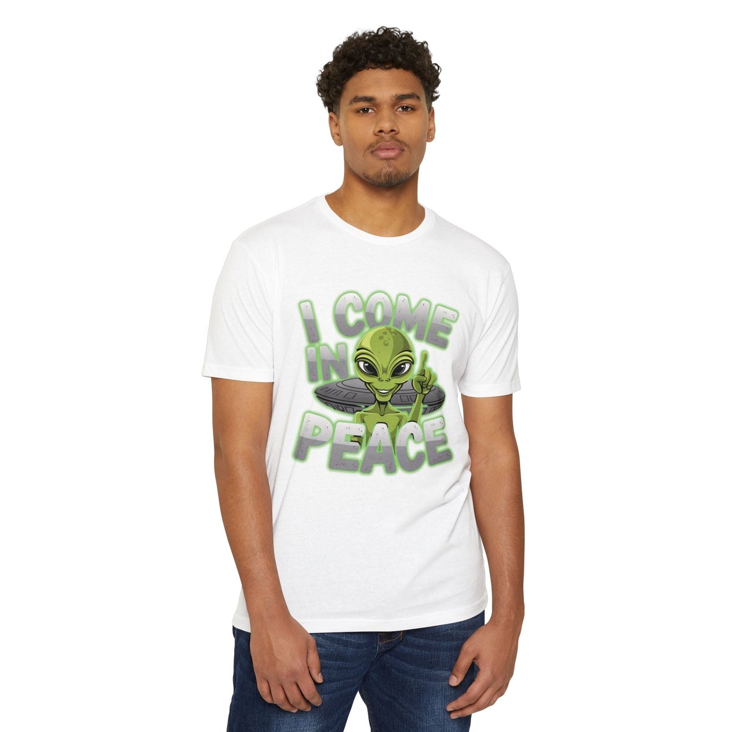 A man in casual wear sports the Alien CVC Jersey T-shirt - I COME IN PEACE, showcasing a green alien graphic along with the text "I Come in Peace," ideal for sci-fi lovers.