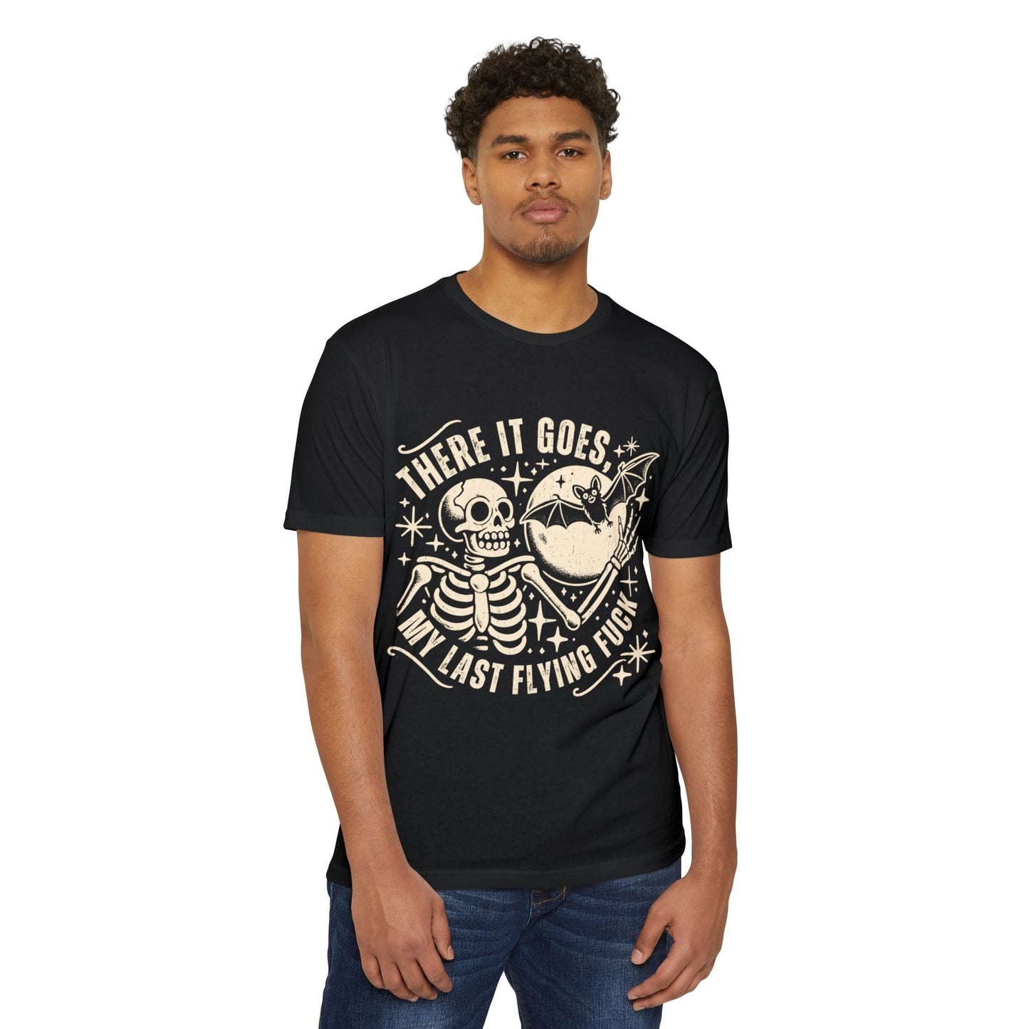 A man is wearing the Unisex T-shirt Skeleton Bat Last F*ck Design, a black T-shirt with a graphic featuring a skeleton and a spaceship that reads, "There it goes, my last flying fuck." Perfect for Halloween parties, his dark humor shines through with this unique statement piece.