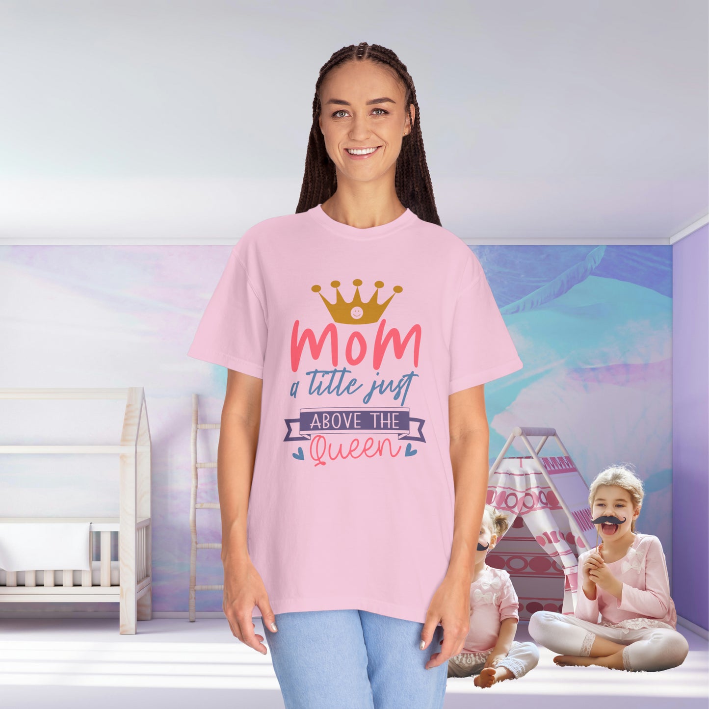 In a vibrant, cozy room, made warm with the quality of the Stylish Comfort Unisex Comfort Colors 1717 Garment-Dyed T-Shirt reading "mom just a little above queen," a woman stands, wearing pink as two children play happily on the floor.