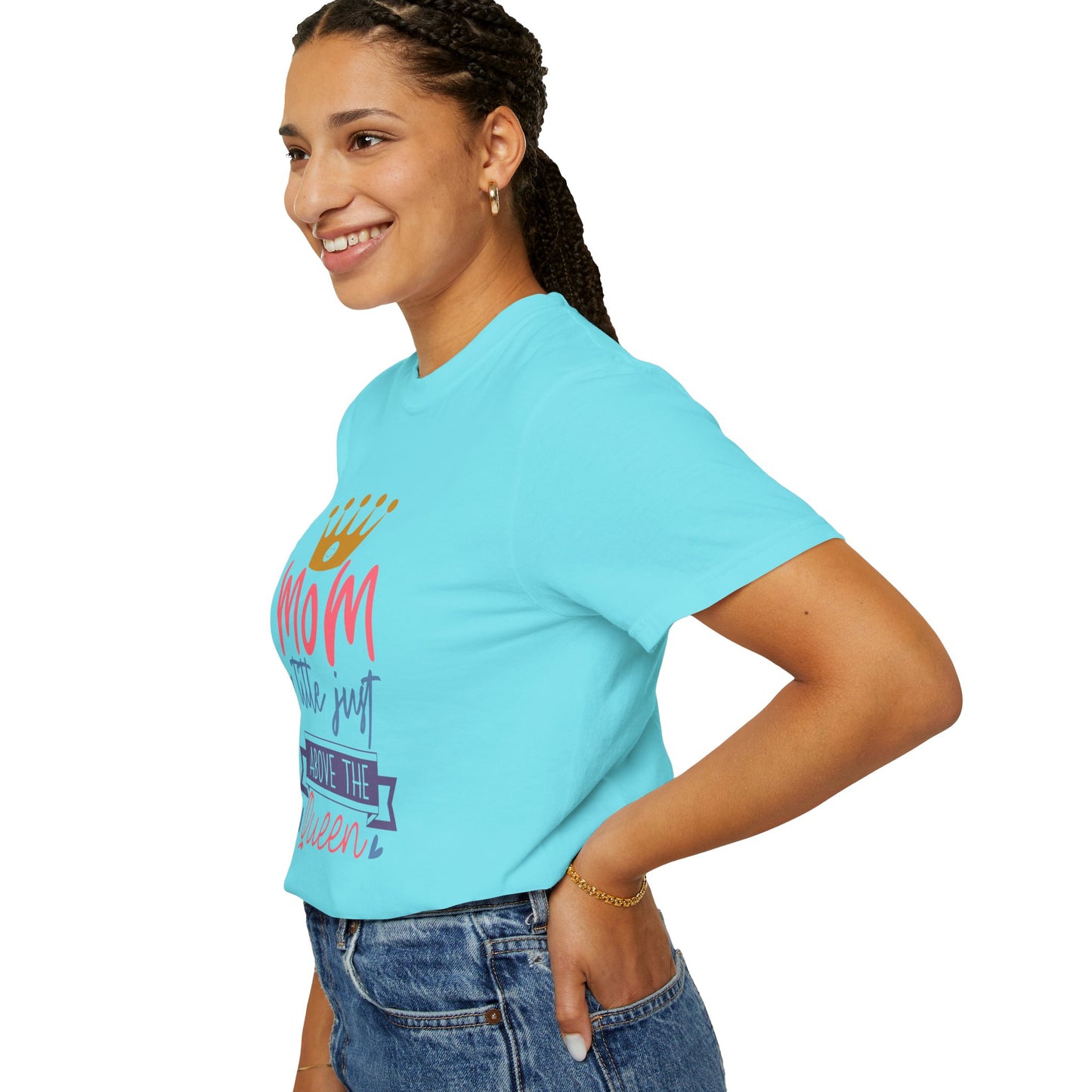 A woman wearing the Stylish Comfort with Unisex Comfort Colors 1717 Garment-Dyed T-Shirt in turquoise, featuring the text "mom just a little above queen" and a crown graphic, smiles and poses against a white background. The ring-spun cotton tee pairs perfectly with her jeans and braids.