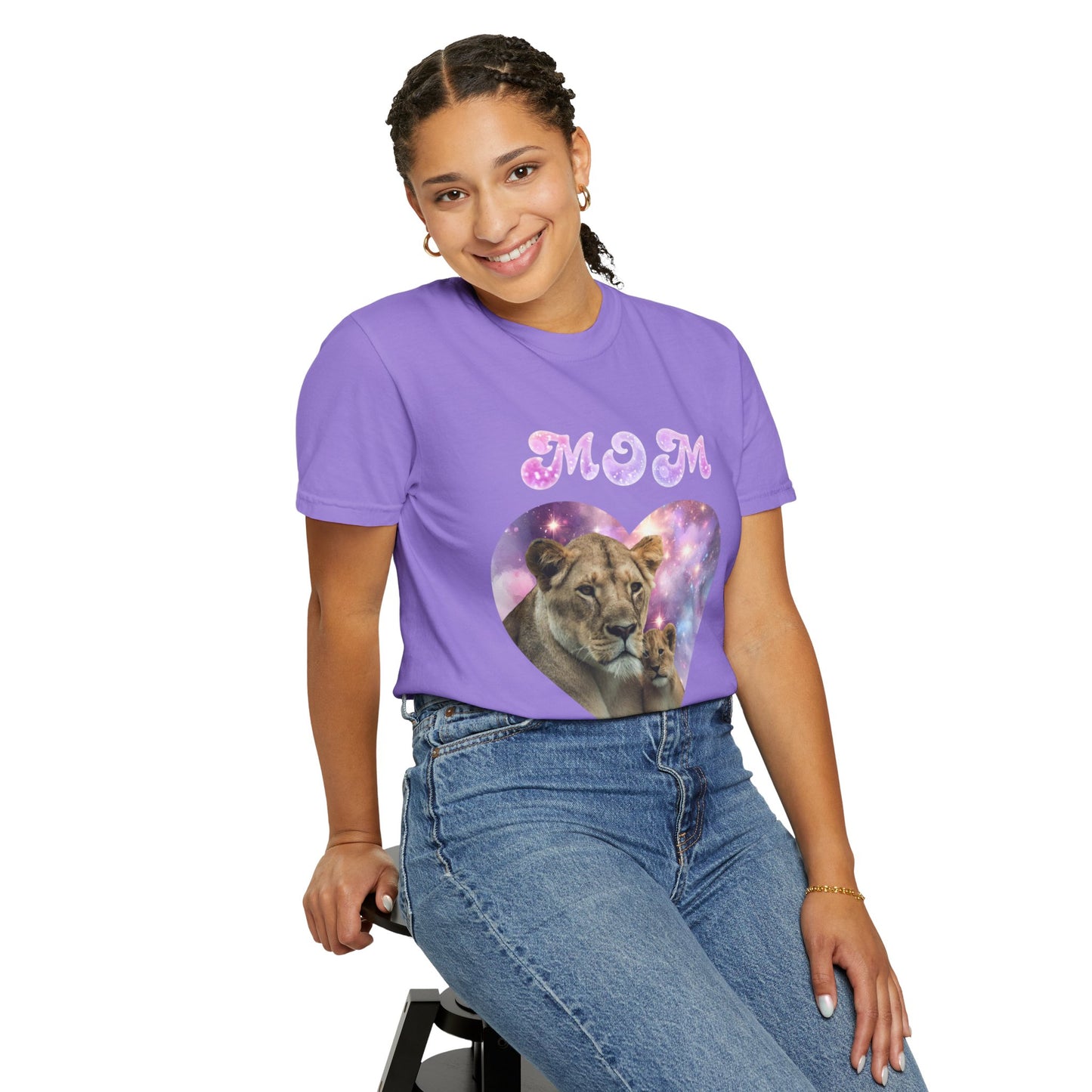 Woman in a purple "Stylish Comfort with Unisex Comfort Colors 1717 Garment-Dye- T-shirt- Heart of the Cosmos: Mom's Lioness Legacy" with lion and cub images, smiling and sitting on a black stool, against a white background.