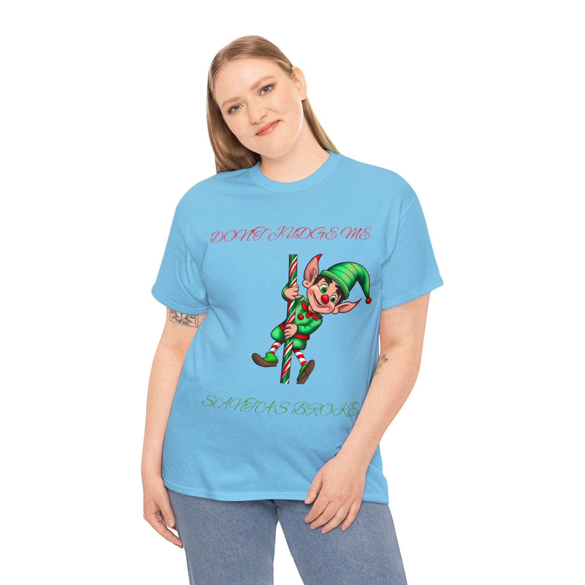 A person wearing the Unisex Heavy Cotton "Don't Judge Me Elf" shirt, featuring a classic fit in blue and made from 100% cotton, displays an elf holding a candy cane with the text "DON'T JUDGE ME SANTA'S BROKE.