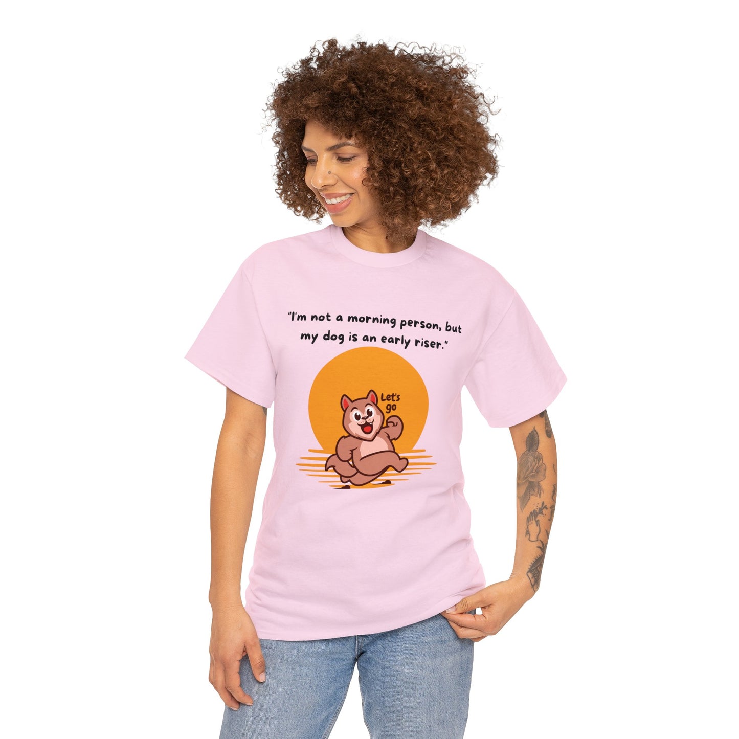 A person with curly hair is sporting a Classic Fit pink Unisex Heavy Cotton Tee, made from 100% sustainable cotton, adorned with a cartoon dog and the slogan, "I'm not a morning person; but my dog is an early riser.