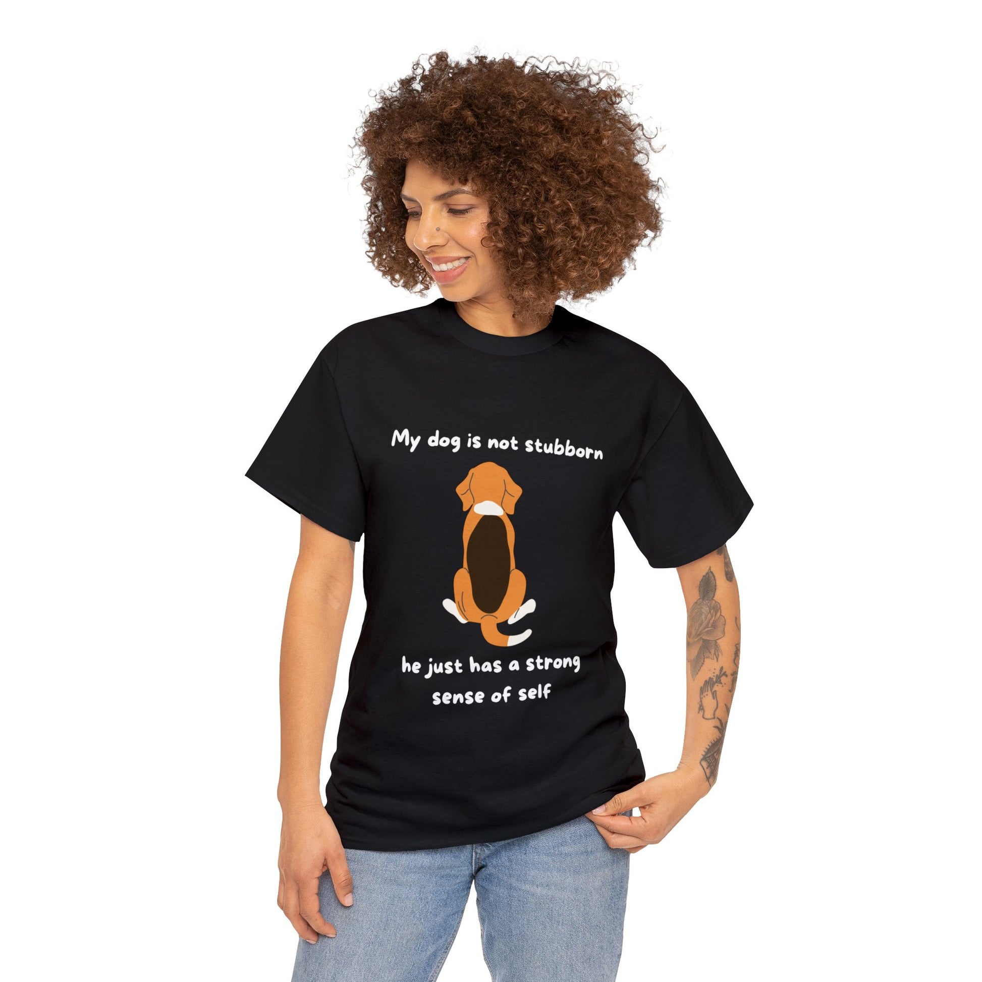 A person is wearing the Unisex Heavy Cotton Tee - MY DOGS NOT STUBBORN- BEAGLE2, a black T-shirt showcasing an illustration of a dog accompanied by the text: "My dog is not stubborn, he just has a strong sense of self." This tee offers a classic fit and is made from 100% cotton with an emphasis on sustainable production practices.