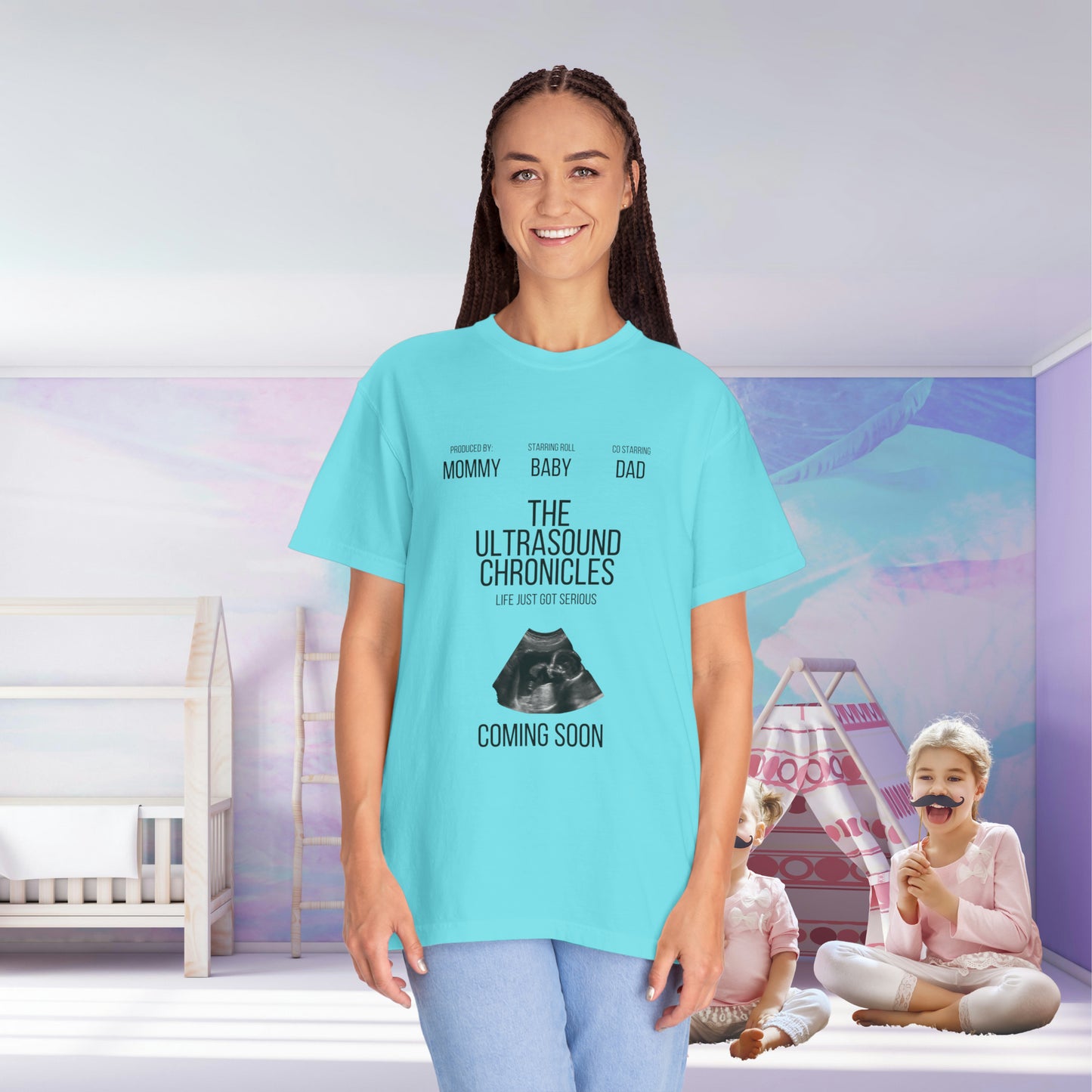 A woman in a Stylish Comfort with Unisex Comfort Colors 1717 Garment-Dye- T-shirt- The Ultrasound Chronicles smiling, with text "the ultrasound chronicles" on it, and two children playing in a softly-colored nursery room background.