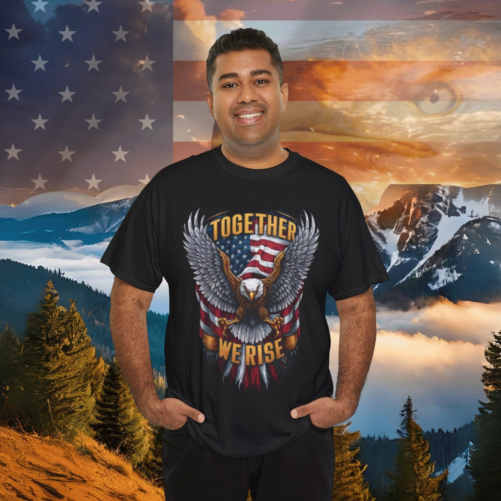 A person wearing an "AMERICA - FLAG AND EAGLE - TOGETHER WE RISE" Unisex Heavy Cotton Tee, crafted from sustainably sourced cotton, stands in front of a backdrop featuring mountains and an American flag.