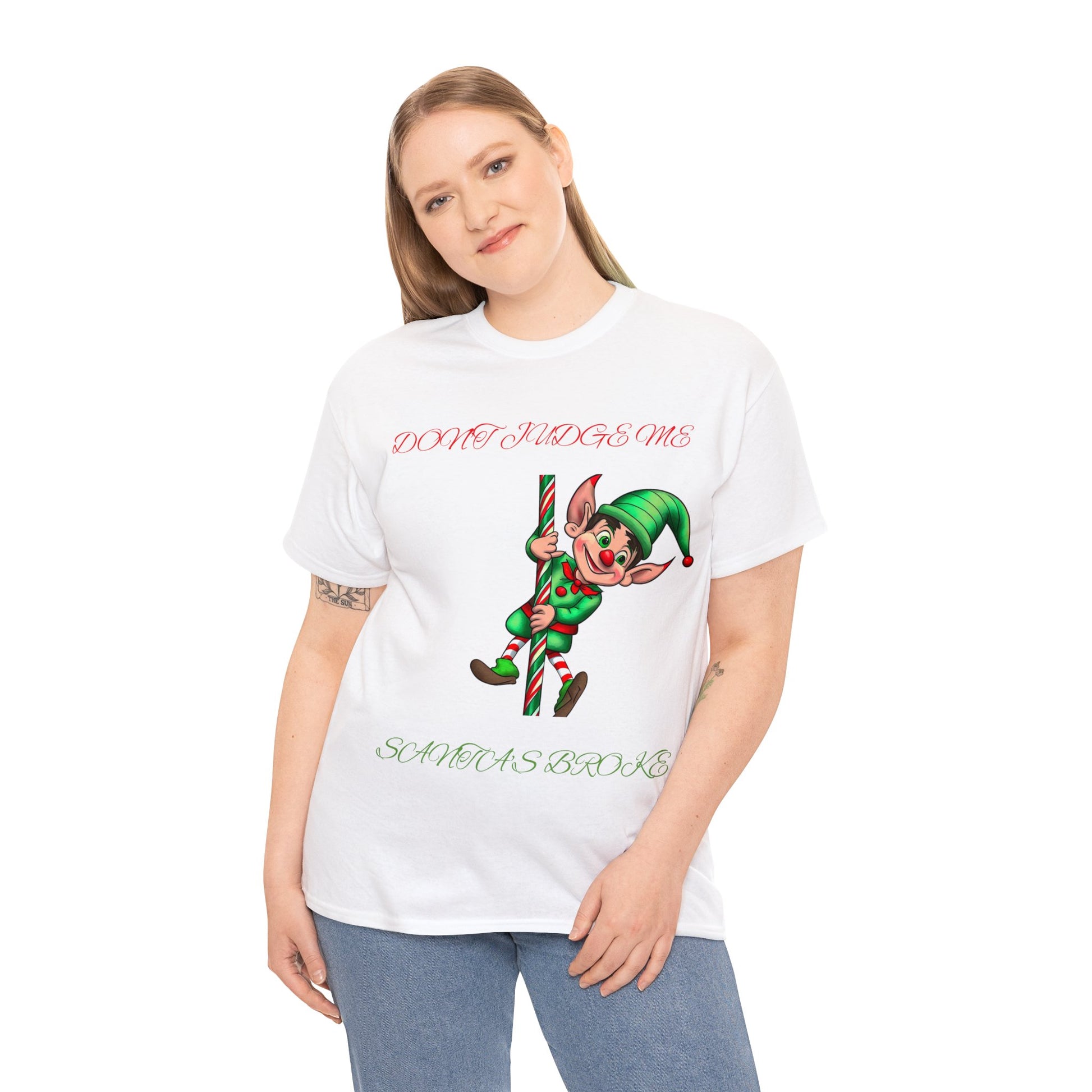 A person wearing a Unisex Heavy Cotton- Don't Judge Me Elf T-shirt, designed in classic fit with 100% cotton. It features an elf holding a candy cane and the text "DON'T JUDGE ME SANTA HAS BOTOX," making it perfect for spreading holiday cheer with humor and sustainability.