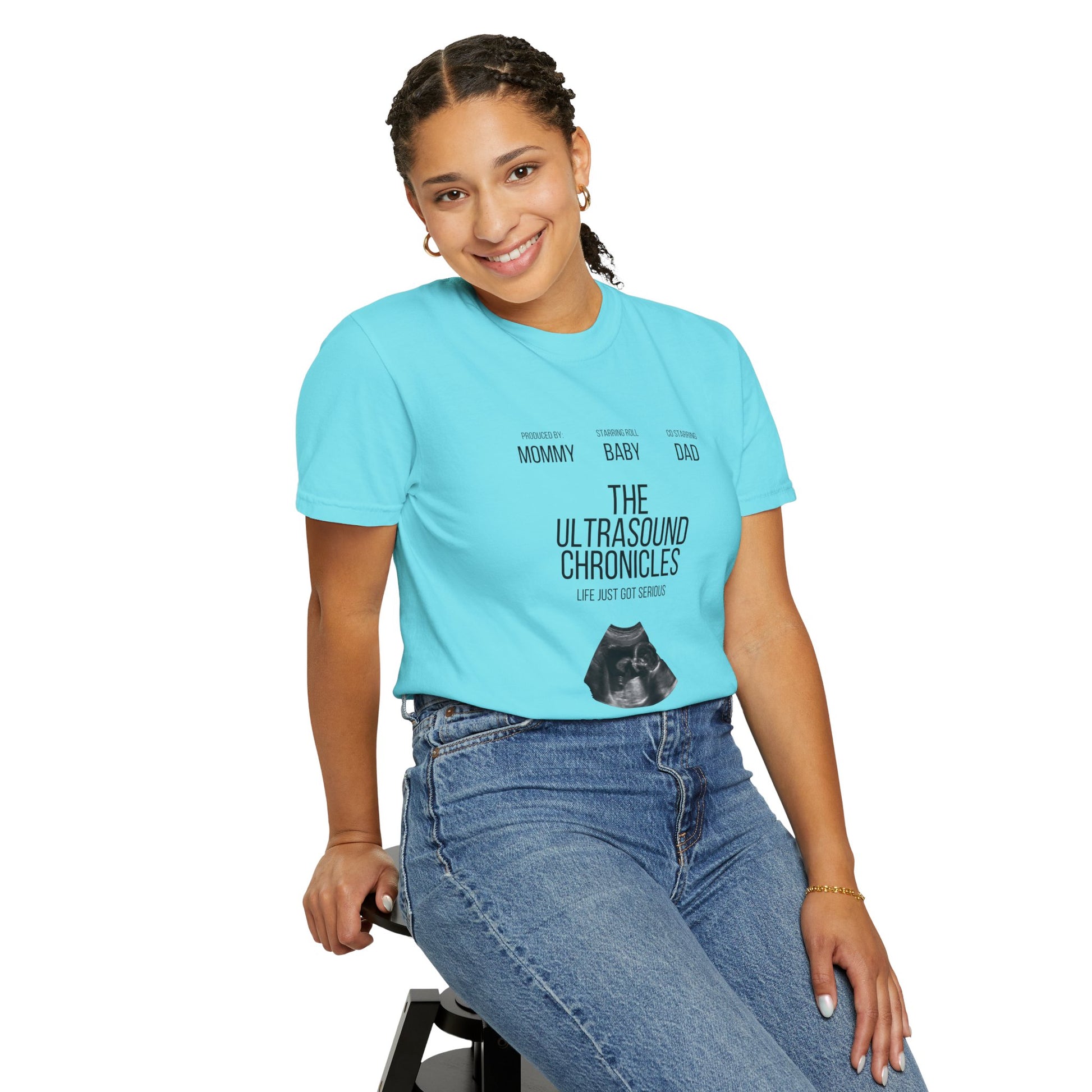 A young woman wearing a Stylish Comfort with Unisex Comfort Colors 1717 Garment-Dye- T-shirt- The Ultrasound Chronicles and jeans, smiling and sitting on a stool.