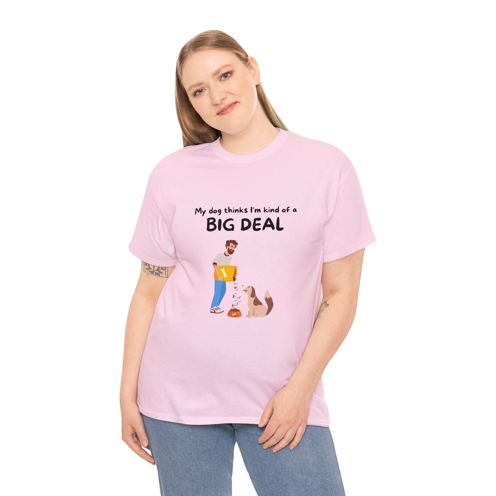 A proud dog enthusiast wears a pink Unisex Heavy Cotton Tee with the message "MY DOG THINKS IM A BIG DEAL," showcasing a seamless design with a cartoon of a person and their dog.