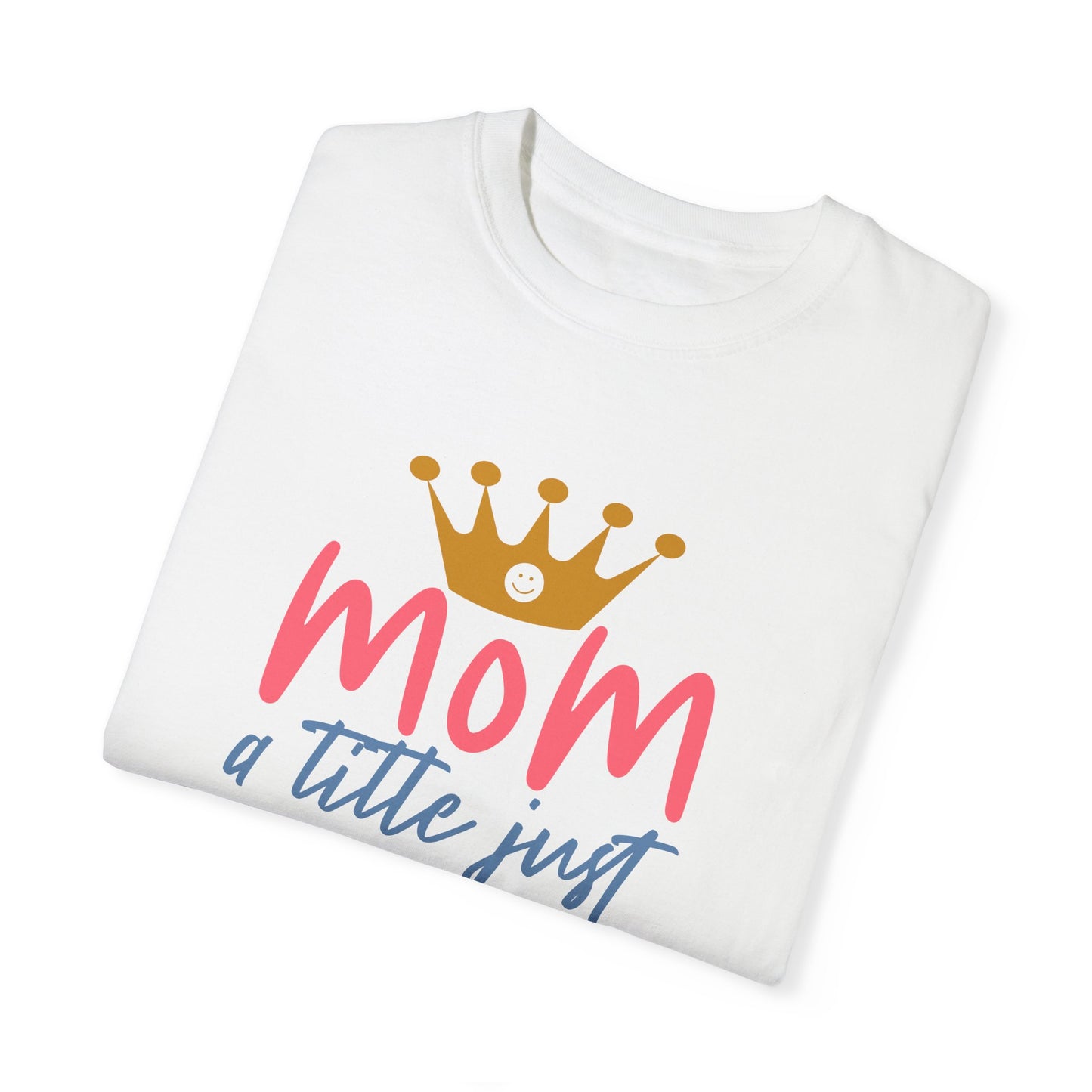 White folded t-shirt crafted from ring-spun cotton, adorned with a golden crown above the pink word "mom." Beneath, the text reads "just a little above queen." This garment-dyed tee embodies quality and style in line with the Stylish Comfort of Unisex Comfort Colors 1717 aesthetics.