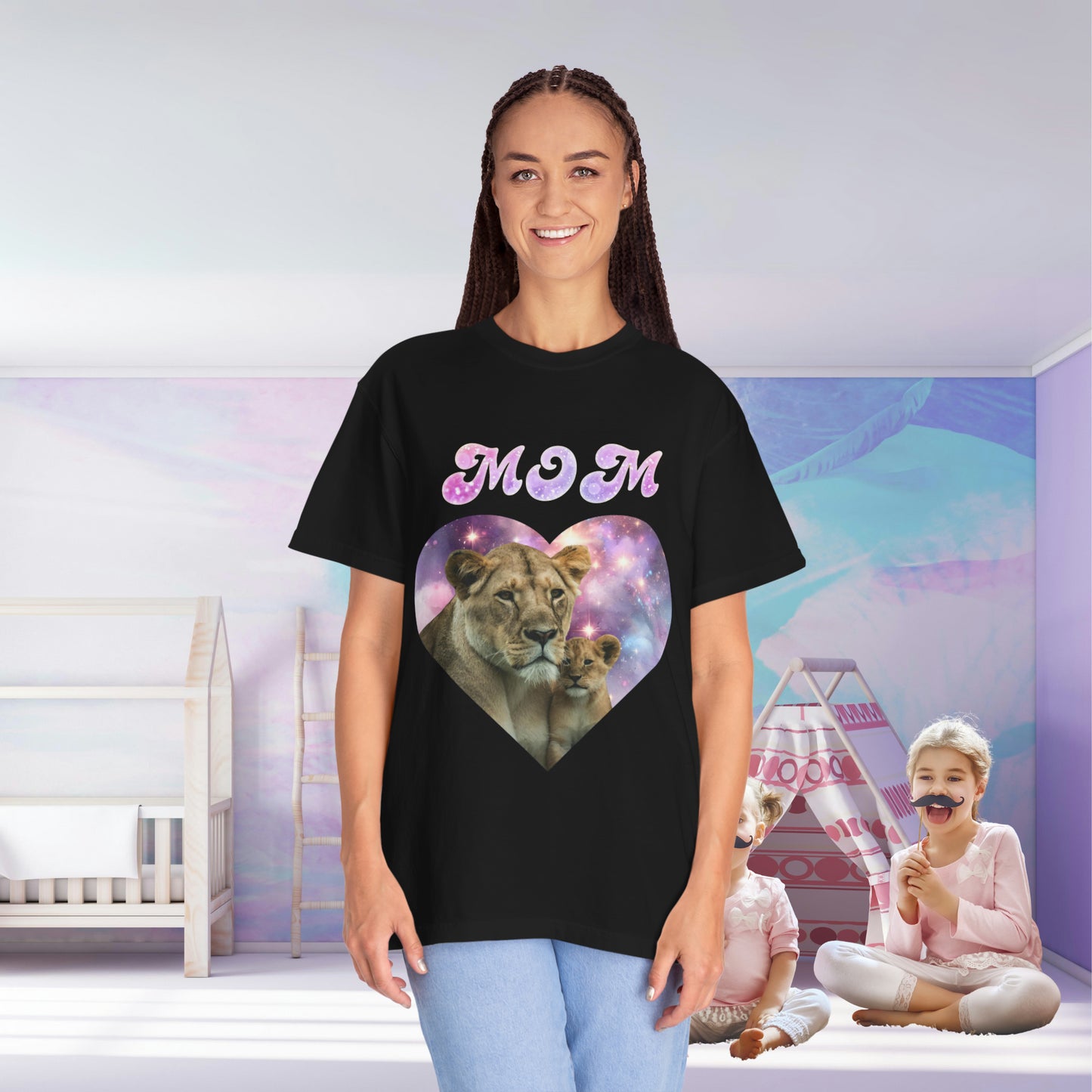 A woman in a black Stylish Comfort with Unisex Comfort Colors 1717 Garment-Dye- T-shirt- Heart of the Cosmos: Mom's Lioness Legacy design stands smiling in a room with a child playing in the background.