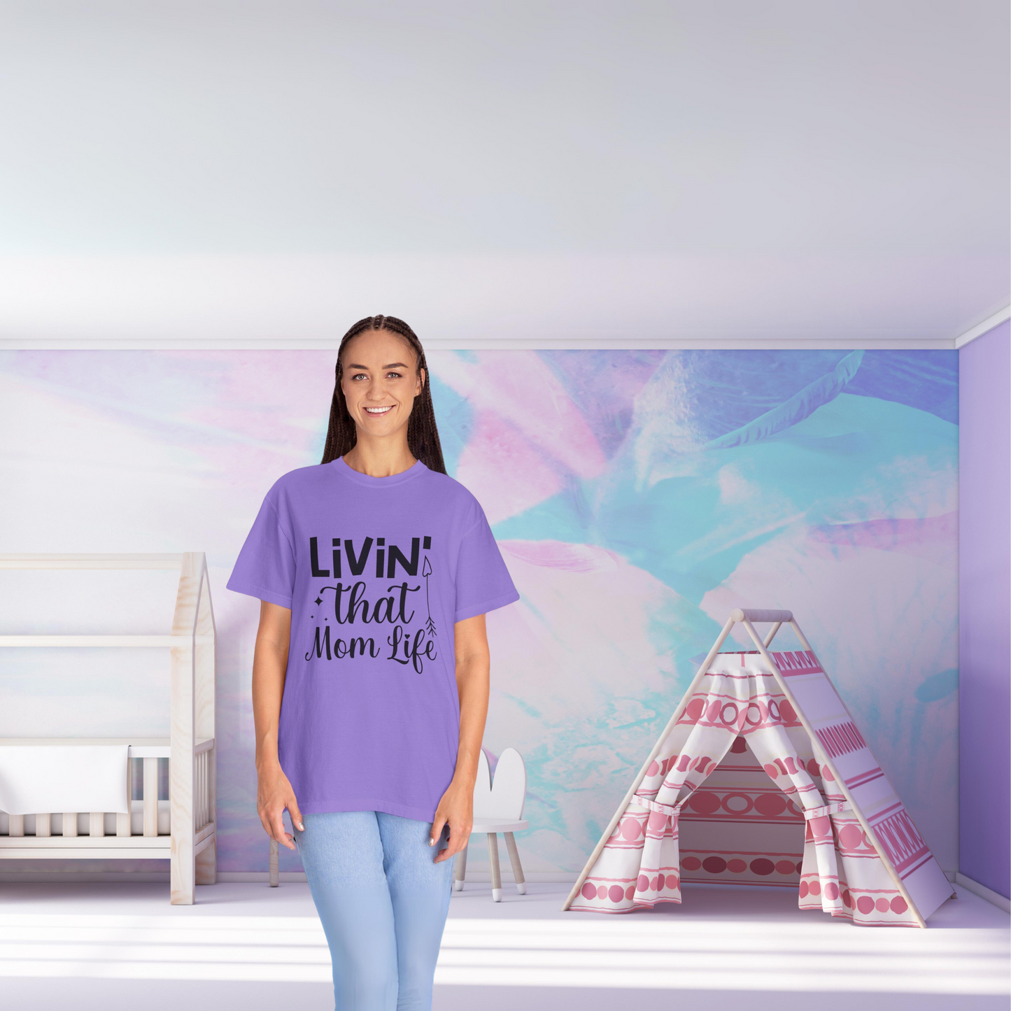 A person wearing a purple Unisex Comfort Colors 1717 Garment-Dyed T-Shirt, styled for living that mom life, stands in a pastel-themed room with a crib and a play tent.