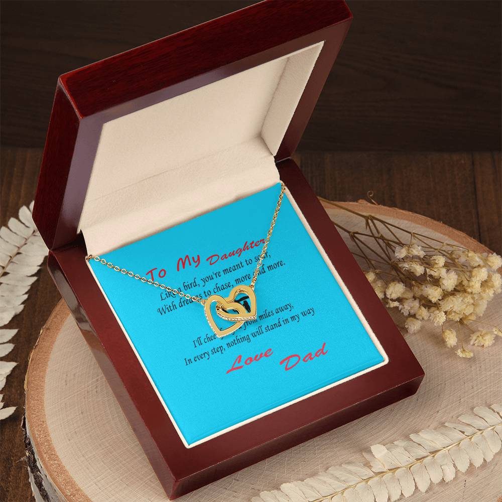 An Interlocking Hearts Necklace- Father Daughter Like a Bird in a wooden box with a blue note inside, inscribed with the message "To My Daughter... Love Dad." The box rests on a wooden surface adorned with dried flowers, an ideal gift for Father's Day.