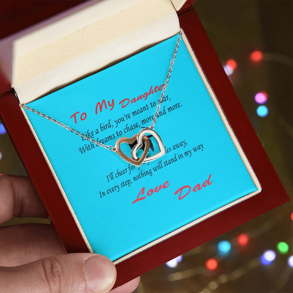 A silver heart-shaped pendant necklace in an open box with a dedication that reads, "To my daughter" from "Love Dad" on an aqua blue card. This heartfelt gift for Dad will make Father's Day unforgettable. Interlocking Hearts Necklace - Father Daughter Like a Bird.