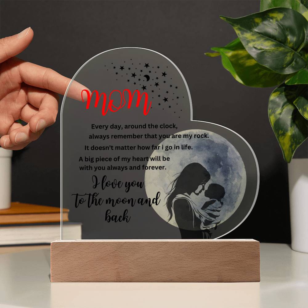 A person touching the "Mom, you are my rock, i love you to the moon" acrylic heart plaque with wooden base with a printed design.