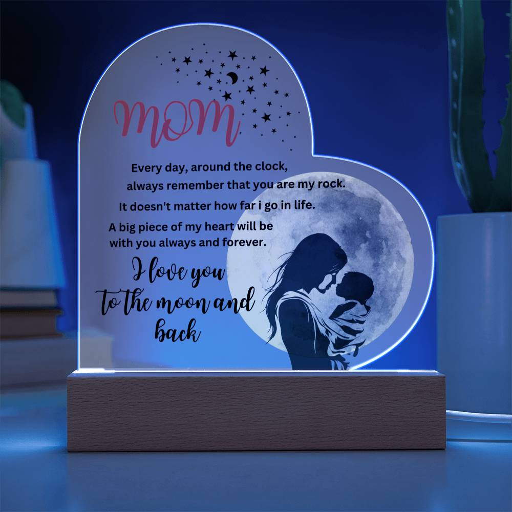 This "Mom, you are my rock, i love you to the moon" acrylic heart plaque with wooden base features a printed design of a woman and a moon, making it the perfect gift.