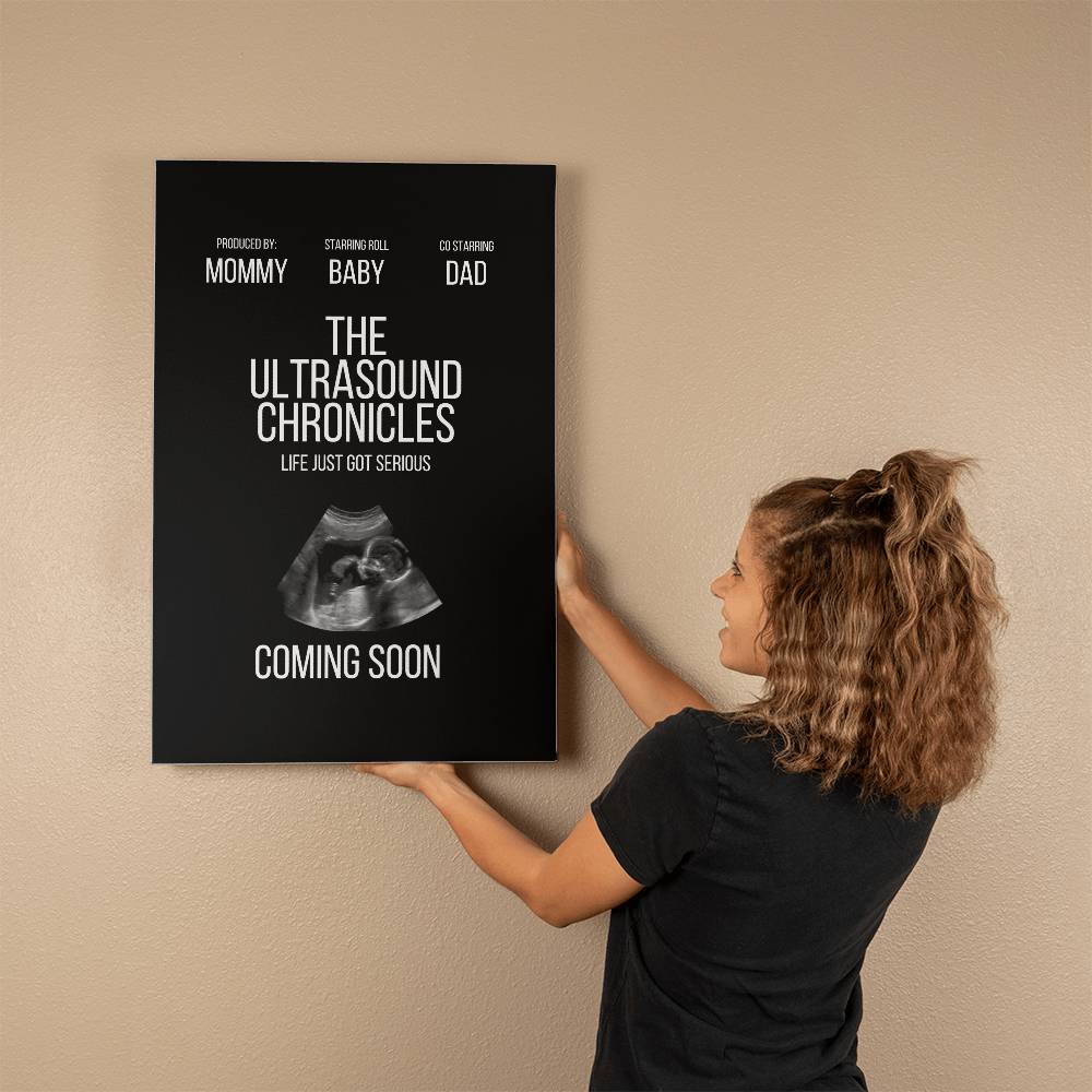 A new mom hanging a Gallery Wrapped Canvas (2:3) titled "The Ultrasound Chronicles" featuring an ultrasound image and text "Coming Soon" on a wall.