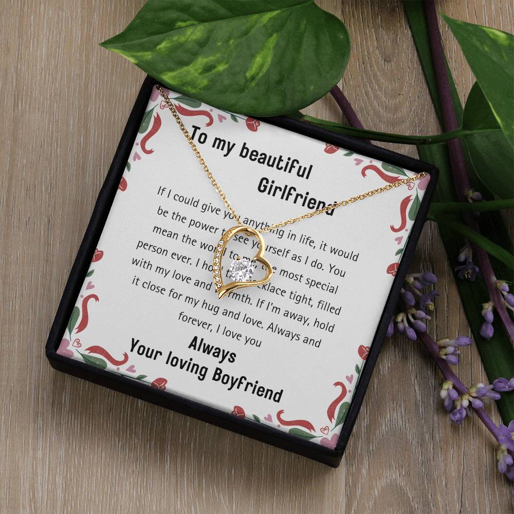 The 20240114_112056_0001 Forever Love Necklace, crafted in a gold heart shape featuring a brilliant cubic zirconia finish, is presented on a card with a romantic message and elegantly nestled in a jewelry box adorned with lush green leaves.