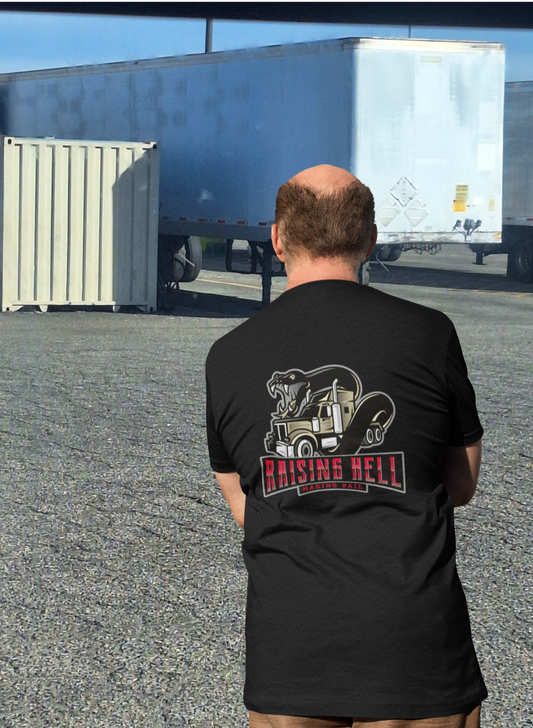 A man wearing a Unisex Softstyle T-Shirt featuring the "Raising Hell" cream long nose with a viper design, made from 100% cotton, stands in front of a shipping container and trailer.